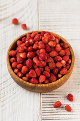 Ripe wild strawberries in a wooden bowl on a white wooden table. Wild berries