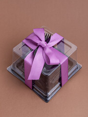 Plastic container for confectionery on brown background. Disposable box for transportation. Festive packaging with ribbon and disposable fork