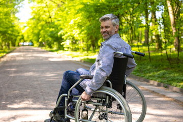 Gray haired disable man in wheelchair spending free time in park.