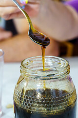 Person pouring honey from spoon into transparent jar, close-up shot.