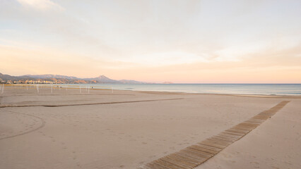 Big sea beach at sunset and mountains on the horizon. Empty sea beach with yellow sand. Pink sunset...