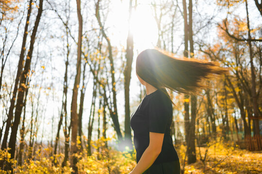Cute young woman with long fluffy hair dancing in a park at sunset. Beautiful young woman with brown hair dance in a forest at sunset. Freedom and season nature concept. Soft focus