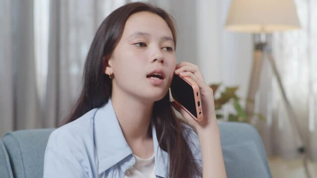 Close Up Of Asian Teen Girl Talking On Smartphone While Sitting On Sofa In The Living Room At Home
