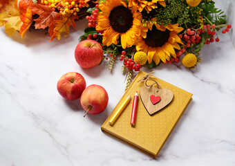 autumn seasonal composition. decorative heart, pencils, book, autumn flowers and apples close up on abstract marble background. fall time concept. copy space. template for design