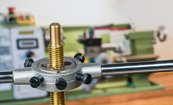 Closeup a steel metalworking die at cutting screw thread on a brass rod. Sharp hand threading tool in tap wrench with black metal bolts on blurred workshop background with green lathe. Chip machining.