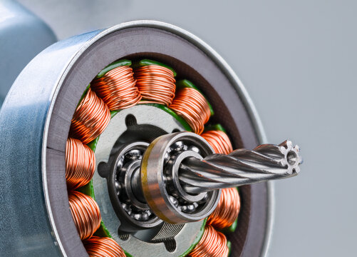 Closeup of electric motor rotor with worm gear, ball bearing and inductors on gray background. Copper wire winding on electromagnetic coils with metal sheets inside steel bushing of electrical engine.