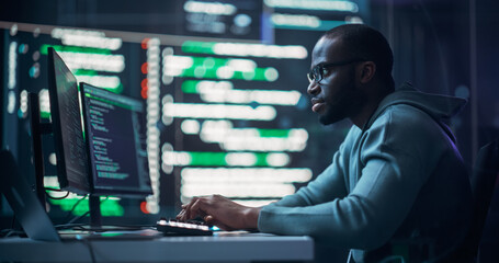 Focused Black Male Programmer Working in Monitoring Room, Surrounded by Big Screens Displaying...