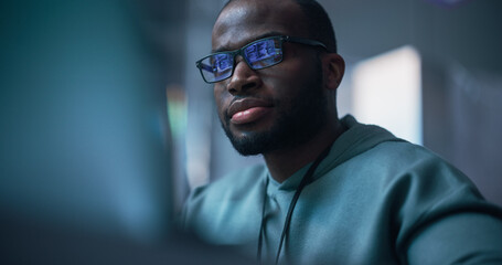 Fototapeta na wymiar Close Up Portrait of Black Man Working on Computer, Lines of Code Language Reflecting on his Glasses. Male Programmer Developing New Software, Managing Cybersecurity Defence Project.