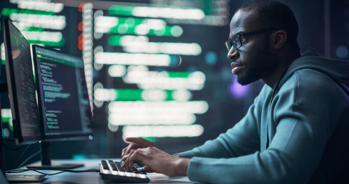 Black Male Programmer Working in Monitoring Room, Surrounded by Big Screens Displaying Lines of Programming Language Code. Portrait of Man Creating a Software. Futuristic Coding Concept.