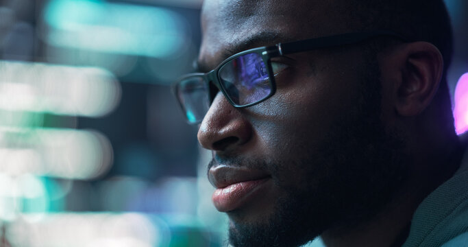 Close Up Portrait of Black Man Working on Computer, Lines of Code Language Reflecting on his Glasses. Male Programmer Developing New Software, Coding, Managing Cybersecurity Project