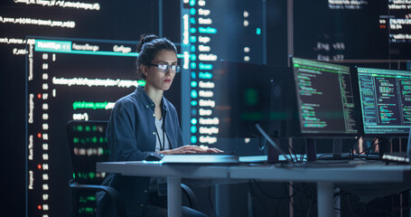 Female Programmer Working in Monitoring Control Room, Surrounded by Big Screens Displaying Lines of...