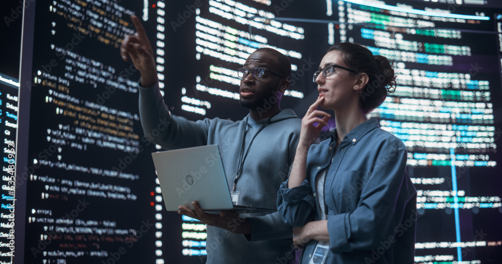 Poster Portrait of Two Diverse Developers Using Laptop Computer, Discussing Lines of Code that Appear on Big Screens Surrounding Them. Male and Female Programmers Creating Software Together and Fixing Bugs