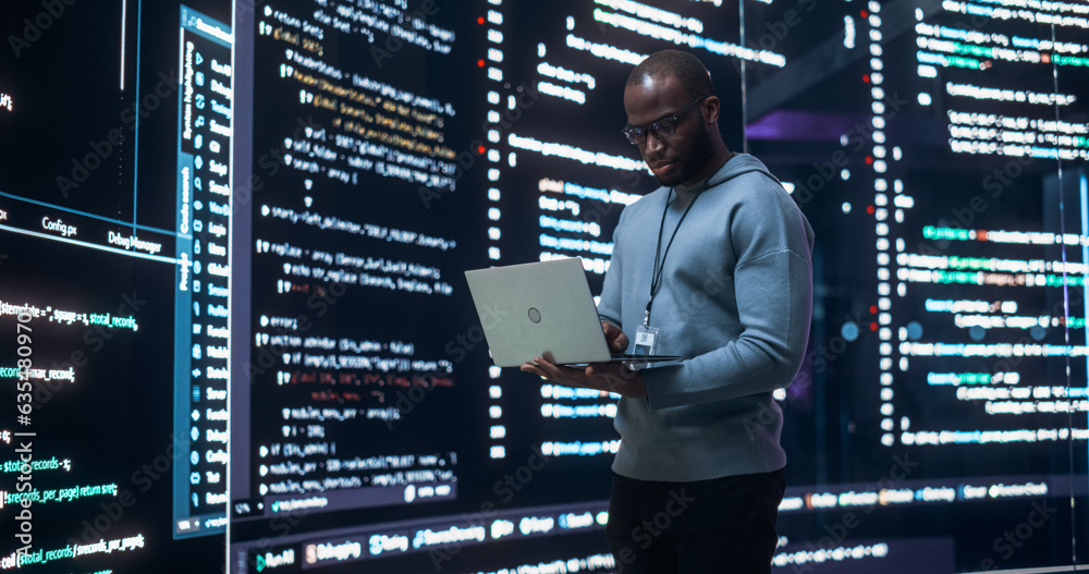 Fototapete Portrait of Young Black Man Working on Laptop Computer, Looking at Big Digital Screen Displaying Back-end Code Lines. Professional Programmer Developing a Big Data Interface Software Project