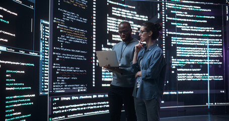 Portrait of Two Diverse Developers Using Laptop Computer, Discussing Lines of Code that Appear on...