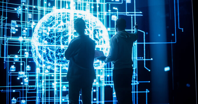 Back View of Two Diverse Colleagues Looking at a Big Screen with Neural Network 3D Visualisation. Professional Computer Data Scientists Discussing and Working on Monitoring Private Information