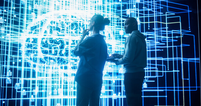 Portrait of Two Diverse Colleagues Looking at a Big Screen with Neural Network 3D Visualisation. Professional Computer Data Scientists Discussing and Working on Monitoring Private Information