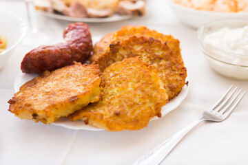 Potato pancakes with fried sausage on white plate