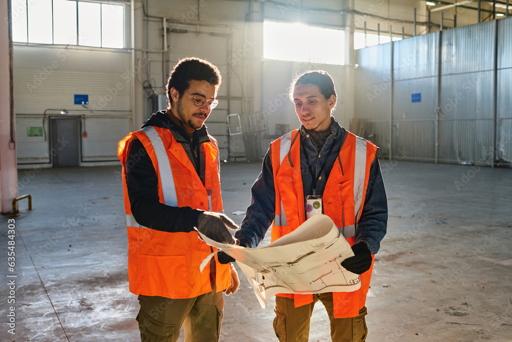 Leinwandbilder Young multiethnic engineer pointing at building plan on blueprint while explaining its points to male colleague during working meeting
