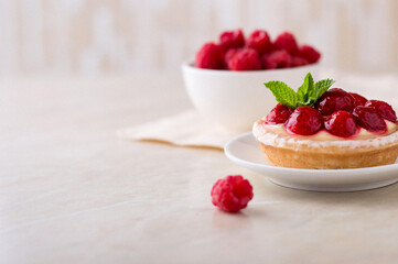 A plate with a custard cake, decorated with raspberries and a mint leaf, on a light background, close up.