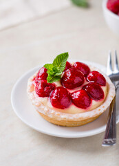 A plate with a custard cake, decorated with raspberries and a mint leaf, on a light background, close up.