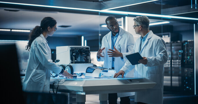 Diverse Team of Industrial Robotics Specialists Gathered Around Table With a Mobile Robot. Engineers In Lab Coats Discussing an Automated Robotic Delivery Assistant with Artificial Intelligence