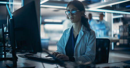 Portrait of a Young Robotics Engineer Using Desktop Computer, Analyzing Robotic Machine Concept in a High Tech Factory. Female Scientist Researching Innovative Ways to Benefit and Progress Humanity