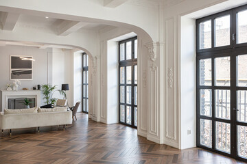 a chic expensive bright interior of a huge living room in a historic mansion with arched arches, columns and white walls decorated with ornaments and stucco.