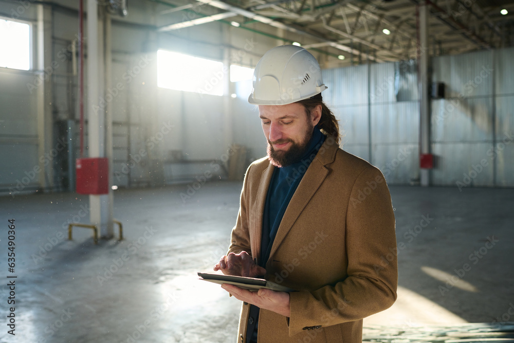 Poster young confident contractor or owner of warehouse scrolling in tablet through online information or d