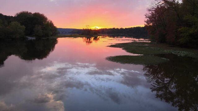 Colorful sunset mirror reflection over still lake with birds and distant interstate travel bridge via backwards arial drone shot 