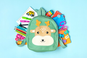 Back to school, education concept Deer green backpack with school supplies - notebook, pens, eraser rainbow, numbers isolated on blue background Top view Copy space Flat lay composition