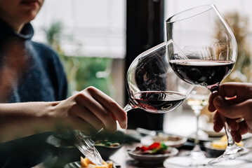 Close up of hands young couple clinking with glasses of red wine at restaurant