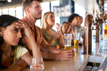 Disappointed Multi-Cultural Group Of Friends In Sports Bar Watching Team Lose Game On TV