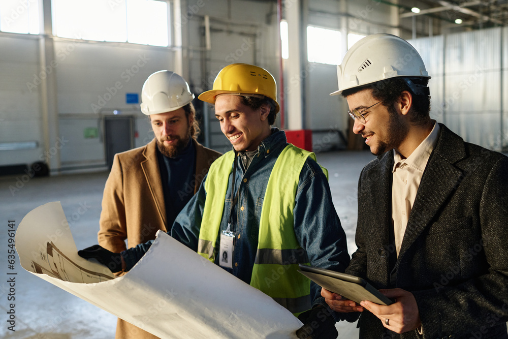 Leinwandbilder side view of three young successful architects discussing points of sketch on blueprint held by man 