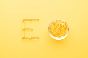 Vitamin E capsules in bowl with alphabet letter E on yellow background. Oil Softgel capsule uses...