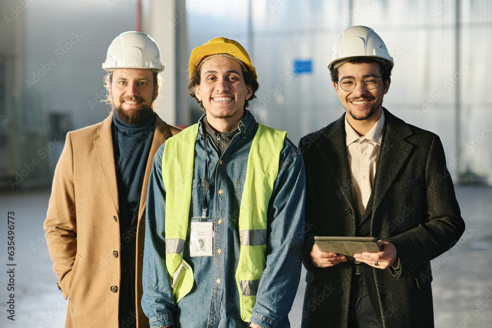 Fototapete three young successful engineers in protective helmets standing in front of camera and looking at yo