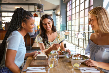 Group Of Female Friends Meeting Up In Restaurant Or Coffee Shop Looking At Mobile Phone