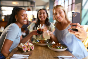 Group Of Female Friends Meeting Up In Restaurant Posing For Selfie On Mobile Phone With Food