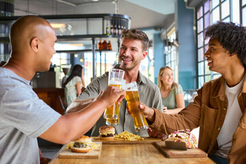 Group Of Male Friends Meeting Up In Bar Eating Burgers And Doing Cheers With Beer