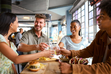 Multi-Cultural Group Of Friends Celebrating Meeting Up In Restaurant Doing Cheers With Water