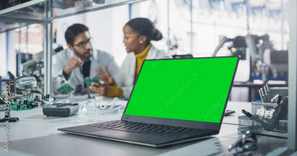 Aufkleber Laptop Computer with Green Screen Mock Up Display Standing on a Table in a Science Class Laboratory. Diverse University Graduates Having a Conversation About Their Electronics Project
