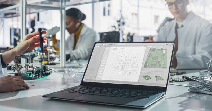 Laptop Computer with Technology Program Display Standing on a Table in a Science Class Laboratory. Diverse Students Practicing Soldering Electronic Components for Their Tech Projects - Powered by Adobe