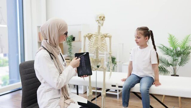 Pediatrician with MRI on tablet consulting girl in clinic