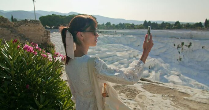 Female tourist take photo of natural travertine pools and terraces or cotton castle in Pamukkale for social media