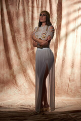 Brunette and elegant woman in egyptian look, pearl top and headdress posing on abstract