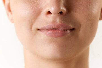 Cropped image of female face, lips and nose over white background. Lip augmentation and...