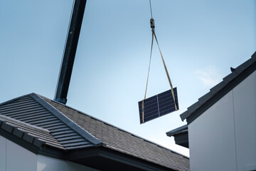The crane is lifting a solar cell panel over the house rooftop for installing on the roof....