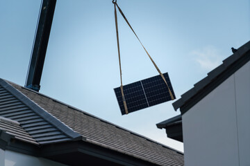 The crane is lifting a solar cell panel over the house rooftop for installing on the roof. Industrial and technology for new alternative energy liftstyle. Selective focus. - obrazy, fototapety, plakaty