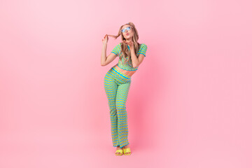 Full body photo of pretty young girl sending air kiss hand touch hair dressed stylish green print outfit isolated on pink color background