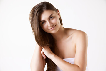 Fototapeta premium Portrait of beautiful brunette young woman with long straight hair, standing in towel against white studio background. Concept of female beauty, hair care, cosmetology and cosmetics, health, ad