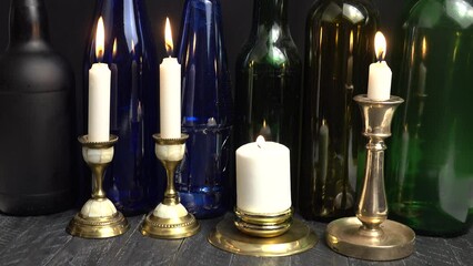 The flame of a burning candle in a brass candlestick is extinguished by a breath of wind. Burning white candles in old vintage brass and bronze candlesticks against the background of glass multicolore - Powered by Adobe